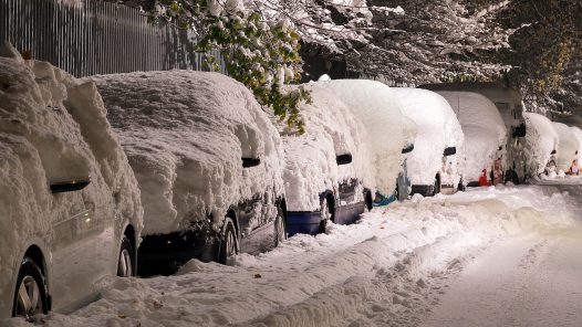 A row of snow-covered cars on a snowy street.
