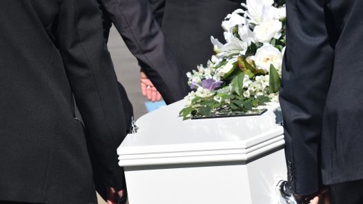 Pall bearers carrying a casket with lilies on it. (https://every1dies.org)