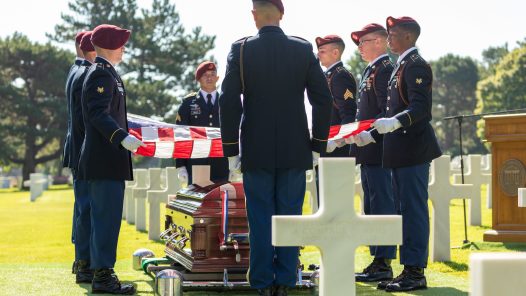 A military funeral detail with a flag held over the casket. U.S. Army Air Forces 2nd Lt. William J. McGowan was laid to rest at Normandy American Cemetery (NOAC) today, nearly 80 years after he was killed during operations in France during World War II (WWII).