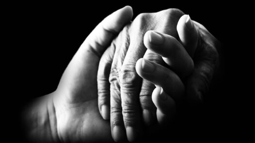 Black and white image of two people holding hands. Learn about caregiving for a partner with dementia in this episode. https://every1dies.org