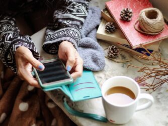 A girl texting on her cell phone. She has a coffee and winter decorations on a table