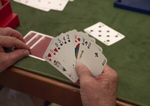 An older person holding a deck of cards. Playing games helps with aging by creating mental challenges and adding social connections.