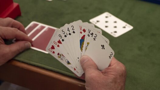 An older person holding a deck of cards. Playing games helps with aging by creating mental challenges and adding social connections.