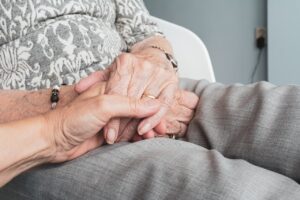 A younger person holding an elder’s hands. We talk about dementia and scams affecting seniors in this episode.