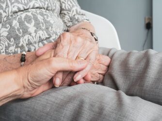 A younger person holding an elder’s hands. We talk about dementia and scams affecting seniors in this episode.