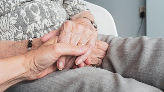 A younger person holding an elder’s hands. We talk about dementia and scams affecting seniors in this episode.