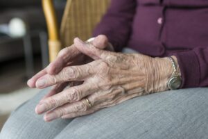 An old woman sitting in a chair with hands touching.