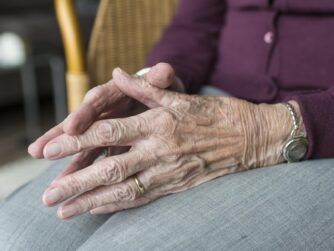 An old woman sitting in a chair with hands touching.