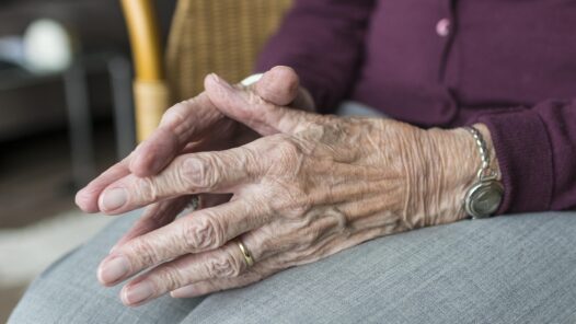 An old woman sitting in a chair with hands touching.