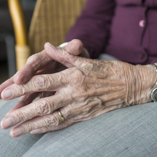 An old woman sitting in a chair with hands touching.