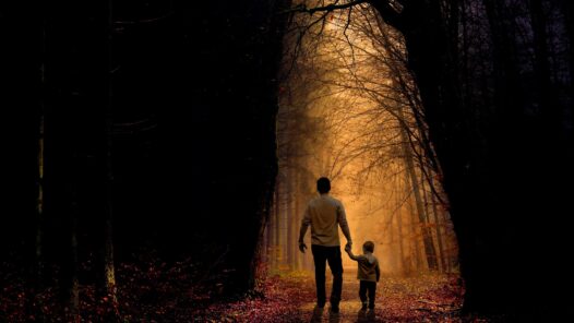 A father walking with his son, holding his hand through a dimly lighted forest. Learn how to talk to your children about death https://every1dies.org