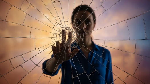 A figure behind glass reaching out, causing it to shatter. We talk about shattering the stigma that can come with a cancer diagnosis in this S6E26 episode.