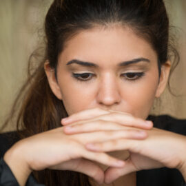 Close-up of face of young Caucasian businesswoman sitting in deep thought with clasped hands