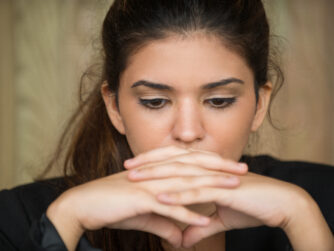 Close-up of face of young Caucasian businesswoman sitting in deep thought with clasped hands