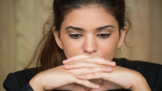 Close-up of face of young Caucasian businesswoman sitting in deep thought with clasped hands