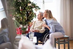 A senior in a wheelchair and a younger woman leaning into her next to a Christmas tree. We talk about Christmas traditions and how things change when a family member has dementia.
