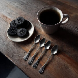 An inviting kitchen table with a cup of coffee and Oreo cookies. Beside the cup is a row of spoons.