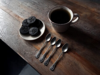 An inviting kitchen table with a cup of coffee and Oreo cookies. Beside the cup is a row of spoons.