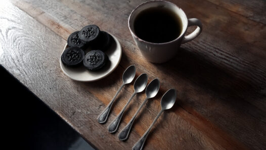 An inviting kitchen table with a cup of coffee and Oreo cookies. Beside the cup is a row of spoons.