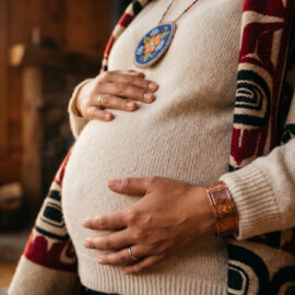 An indigenous mother in warm natural textiles holding her pregnant belly. We talk about indigenous maternal health in this episode.